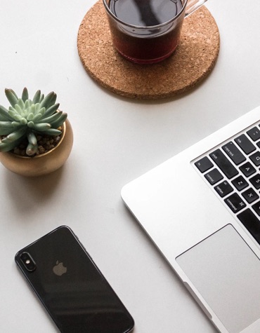 top down photo of a smart phone, a plant, a laptop, and a beverage in a glass mug
